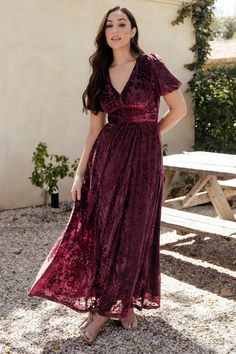 a woman standing in front of a picnic table wearing a burgundy dress with short sleeves