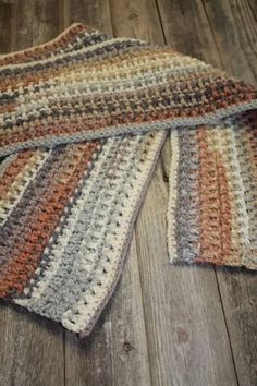 four crocheted dishcloths are laying on a wooden floor, one is orange and the other is gray