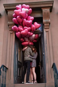 two people standing in an open doorway with pink balloons attached to the door and one person kissing