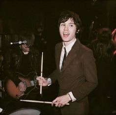 a man in a suit and tie playing the drums with other people behind him at a party