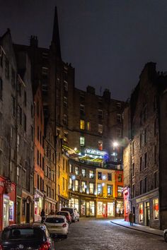 an empty city street at night with cars parked on the side and buildings in the background