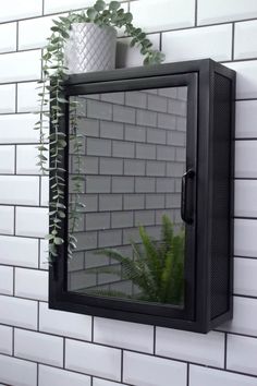 a mirror mounted to the side of a white brick wall next to a potted plant