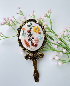 there is a needle - embroidered flower on the key to this brooch that has been placed in front of some pink flowers