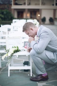 a man kneeling down in front of a white chair with flowers on the ground next to it