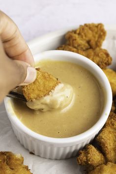 a person dipping something into a bowl of soup with tater tots on the side