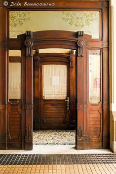 the entrance to an old fashioned building with wooden doors and windows, in front of a tiled floor