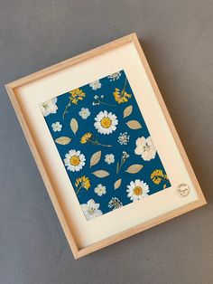 a blue and yellow floral print in a wooden frame on a gray surface with a white border