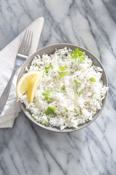 a bowl filled with white rice next to a fork and napkin on a marble surface