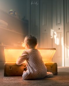 a small child sitting on the floor next to an open suitcase with light coming from it