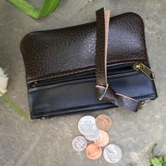 a brown leather purse sitting on top of a cement floor next to some coins and a flower