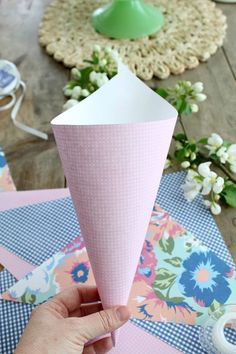 a person is holding a paper cone on a table with flowers and other items around it