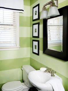 a bathroom with green and white striped walls, black framed pictures on the wall and a sink