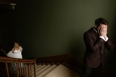 a man in a suit covers his face as he stands next to a woman on stairs