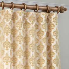 a curtain with gold and white designs hanging on a metal rod in front of a gray wall