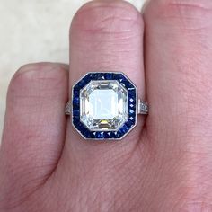 a person's hand holding a ring with an emerald and blue diamond in it