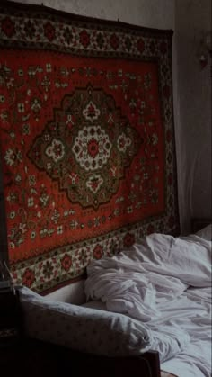 an unmade bed is in front of a large rug on the wall behind it