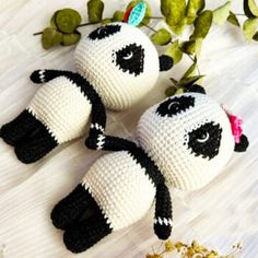 three crocheted panda bears sitting next to each other on a white surface with green leaves