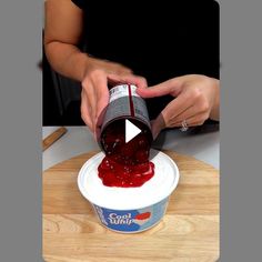 a person pouring ketchup on top of a cake in a cup with the lid down