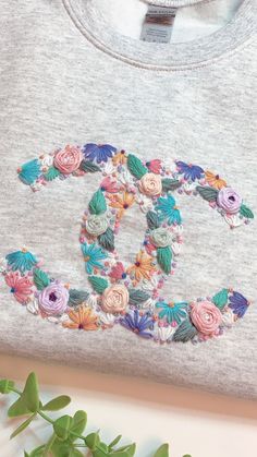 an embroidered t - shirt with flowers and the word chanel on it, sitting next to a plant