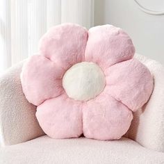 a pink flower shaped pillow sitting on top of a white chair next to a window