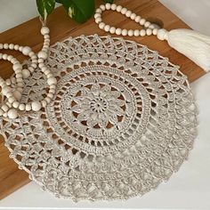 a white doily with beads and tassels on it next to a plant