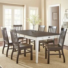 a dining room table with six chairs and a vase on the top of it in front of two windows