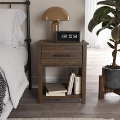 a nightstand with a clock and books on it next to a bed in a bedroom