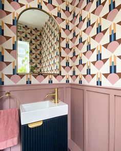 a sink and mirror in a room with wallpaper on the walls, along with a gold faucet