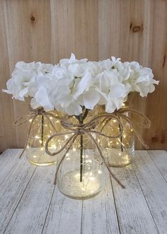 some white flowers are in glass vases with string lights on the top and bottom