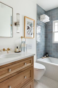 a white toilet sitting next to a bath tub under a window in a bathroom with blue tiles on the walls