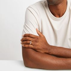 a man with his arms crossed sitting at a table wearing a white t - shirt