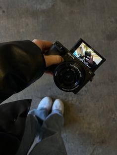 a person holding up a camera to take a picture with their feet on the ground