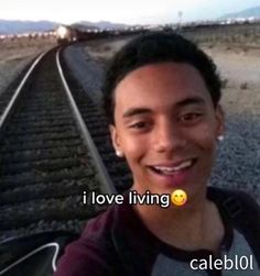 a man is smiling while standing on the train tracks with an emoticive message in front of him