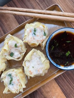 several dumplings with sauce and chopsticks on a wooden tray next to a bowl of soup