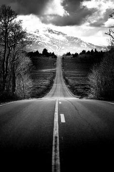 a black and white photo of an empty road with mountains in the backgroud