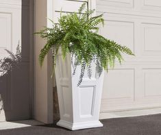 a white planter with a fern in it sitting on the side of a building