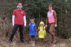 a family dressed up in costumes standing next to each other on a forest floor with pine trees behind them