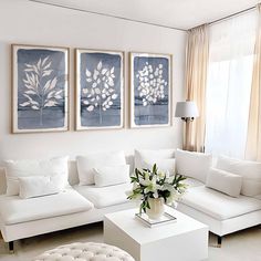 a living room with white furniture and paintings on the wall