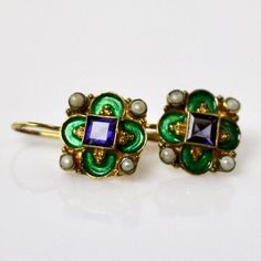 This unique Arts & Crafts Movement design showcases an onyx, iolite, blue topaz, emerald, or garnet set in a cloverleaf of emerald-green or royal blue enamel work, accented with cultured pearl. 24k gold over sterling silver. European back for pierced ears. Size: 3/4 inch. Elegant Enamel Earrings With Gemstones, Elegant Gemstone Earrings With Enamel, Green Jeweled Earrings For Formal Occasions, Green Enamel Jewelry For Wedding, Green Enamel Wedding Jewelry, Formal Green Enamel Jewelry, Elegant Enamel Jewelry With Gemstone, Blue Emerald Gemstone Earrings, Elegant Pierced Enamel Jewelry