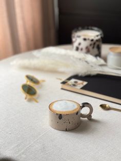 a table topped with two cups filled with liquid and gold spoons next to a pair of sunglasses