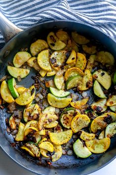 cooked zucchini and squash in a skillet with a striped towel on the side