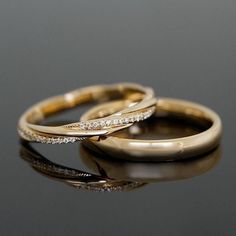 two gold wedding rings with diamonds on top and bottom, sitting on a reflective surface