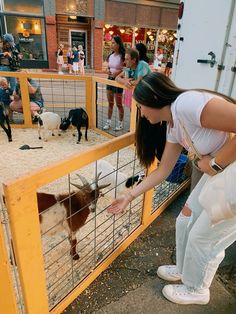 a woman petting a goat in an enclosed area with other people standing around and looking at it