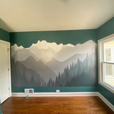 an empty room with mountains painted on the wall and wood flooring in front of it