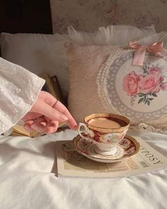 a woman's hand reaching for a cup of coffee on top of a bed