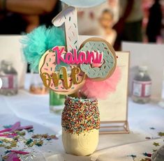 a table topped with a cake and cupcake topper next to a vase filled with sprinkles