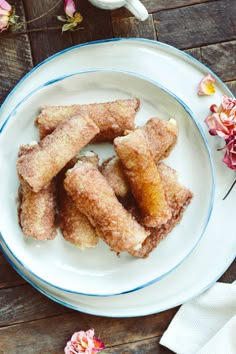 some sugar coated doughnuts on a white plate with pink flowers in the background