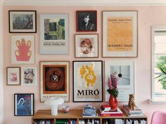 there are many framed pictures on the wall next to a book shelf with books and vases