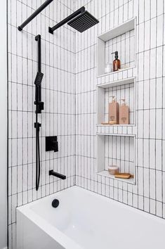 a white bath tub sitting next to a black and white tiled shower head mounted on a wall