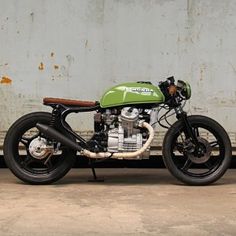 a green and black motorcycle parked in front of a white wall with graffiti on it